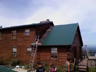 Green metal roof going on a two story log home with ladders set in Bridgewater